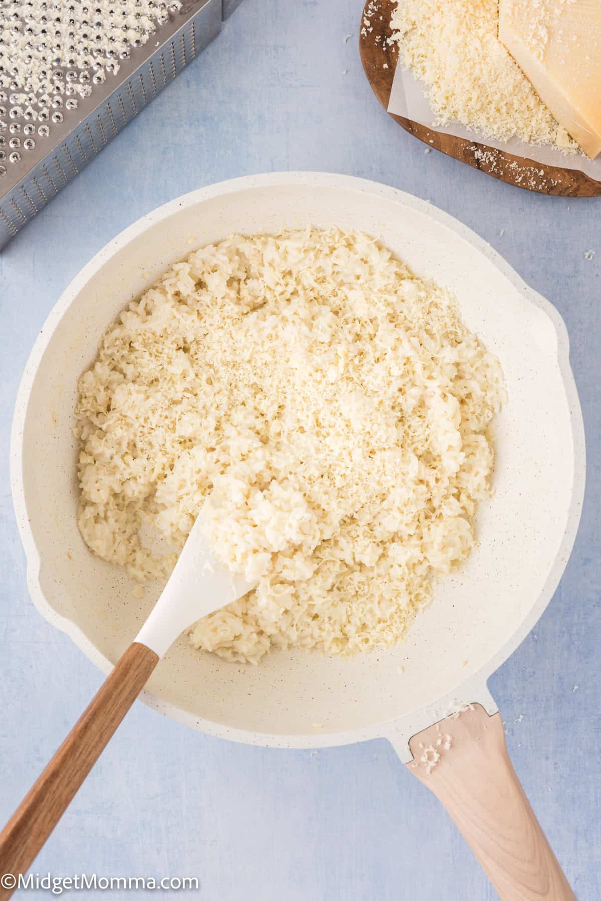 A saucepan containing freshly cooked rice, with a wooden spoon, on a light blue background.