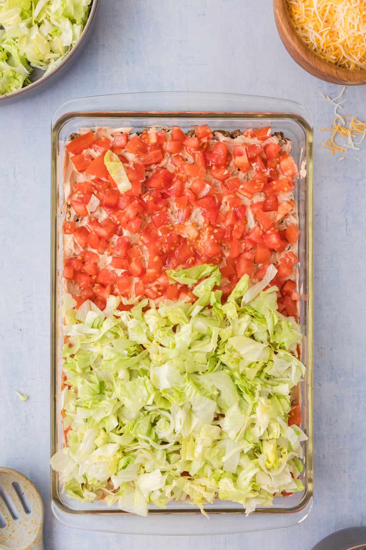 A casserole dish of taco dip topped with shredded lettuce, tomatoes, and cheese.