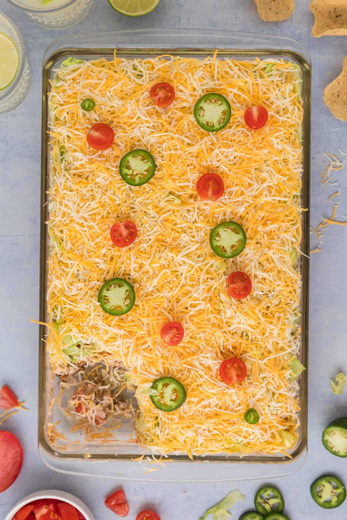 overhead photo of A casserole dish with taco dip topped with shredded cheese, tomatoes, and peppers.