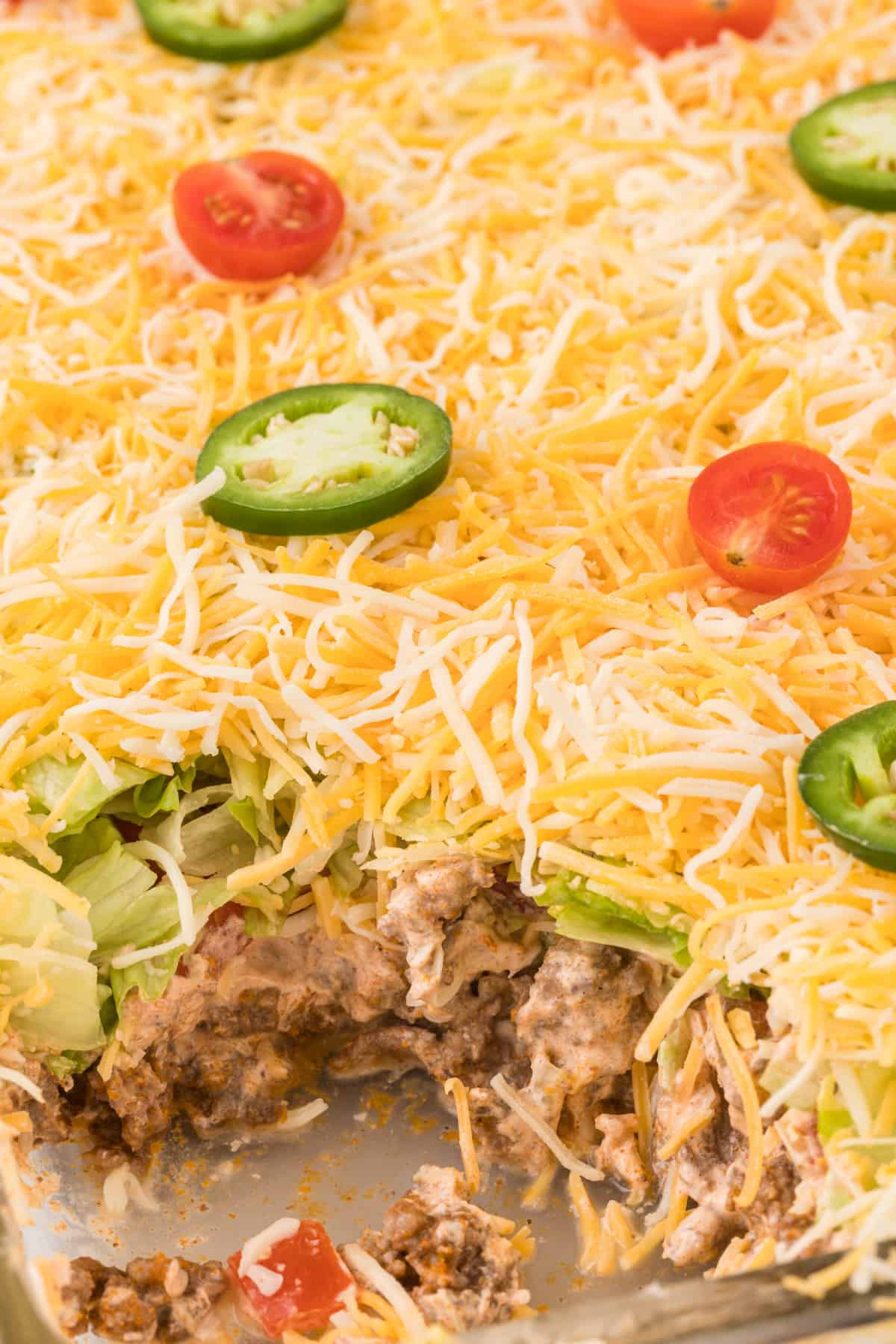 A casserole dish with layered taco dip - topped with shredded cheese, tomatoes, and jalapeno peppers.