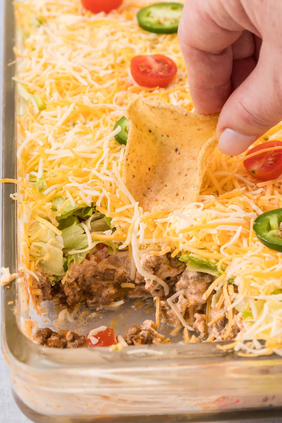 A person dipping a tortilla chip into a casserole dish of layered taco dip