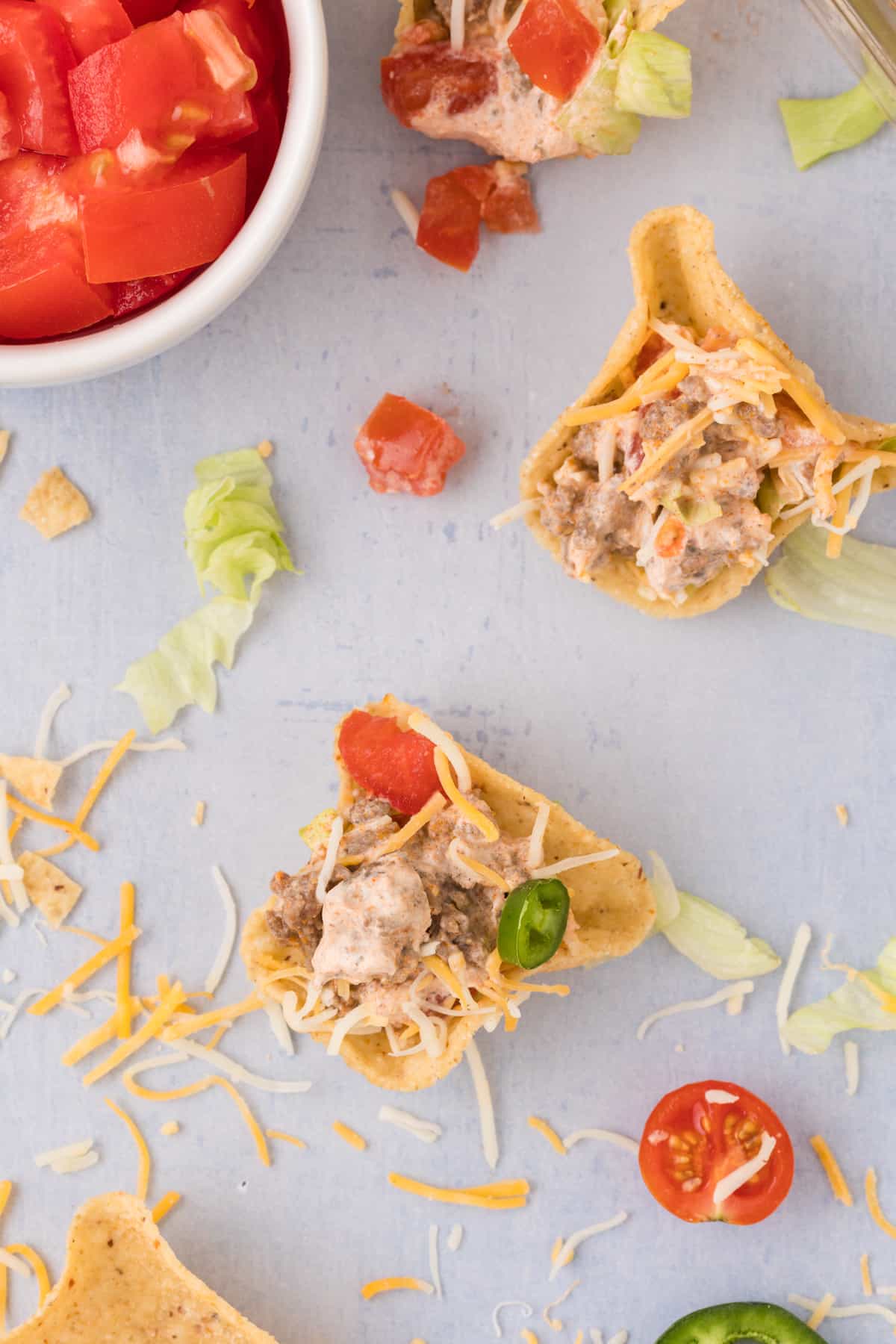 A tortilla chip scoop with taco dip with cheese, tomatoes, and jalapenos.