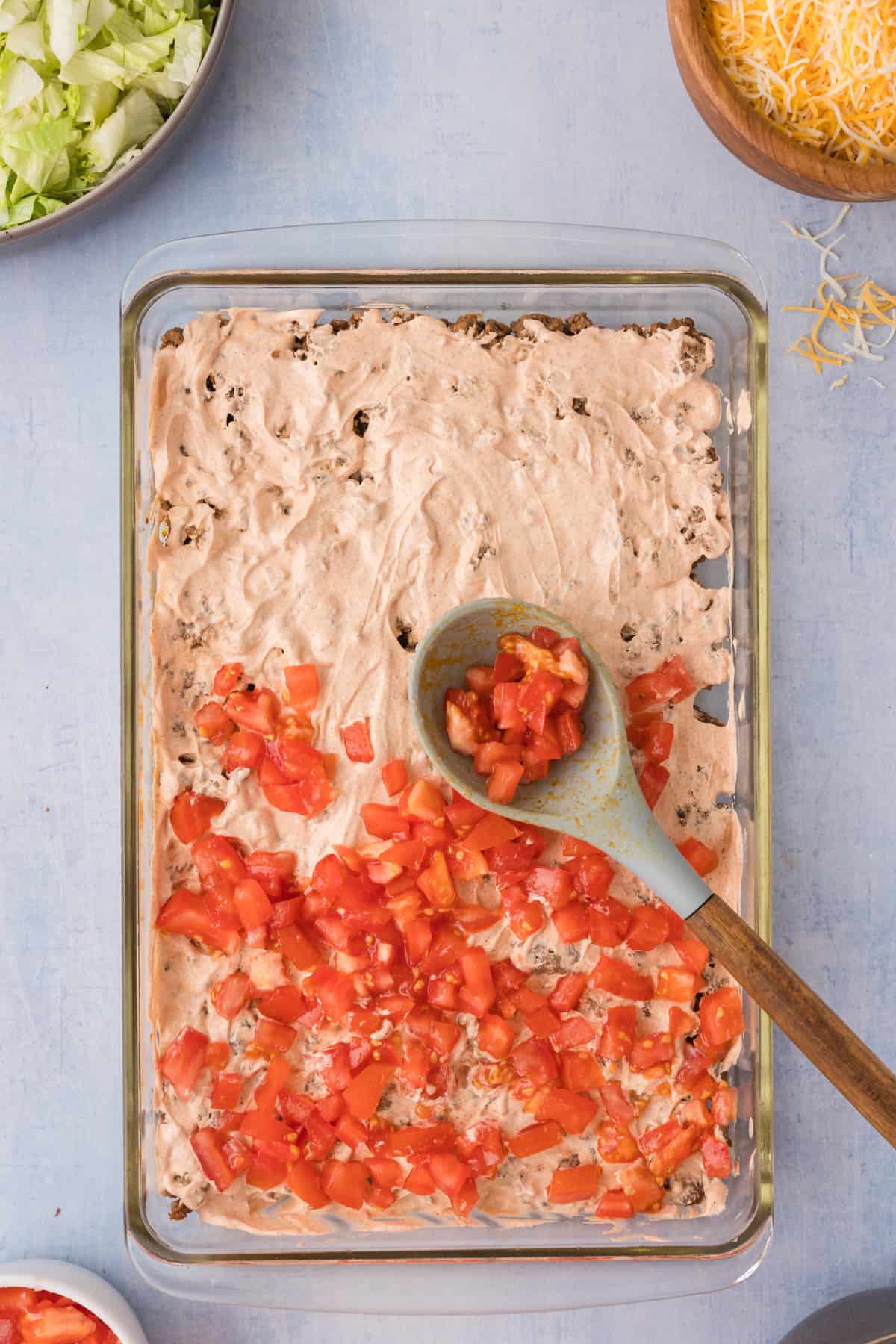 taco dip in a baking dish with tomatoes and cheese.