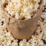 A brown paper bag filled with freshly popped popcorn spilling out onto a wooden surface.