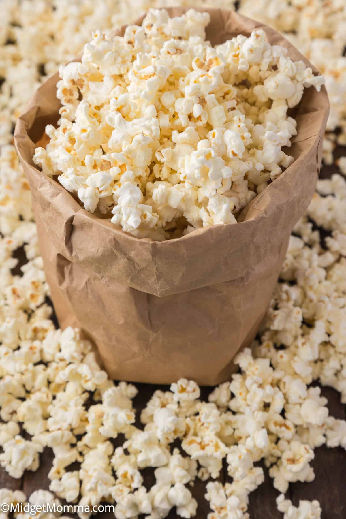 A brown paper bag filled with freshly popped popcorn spilling out onto a wooden surface.