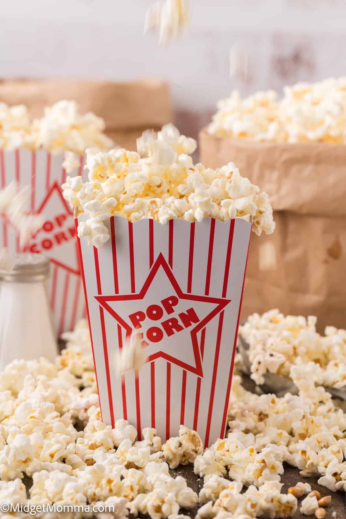 A box of popcorn with scattered kernels around it on a wooden surface.