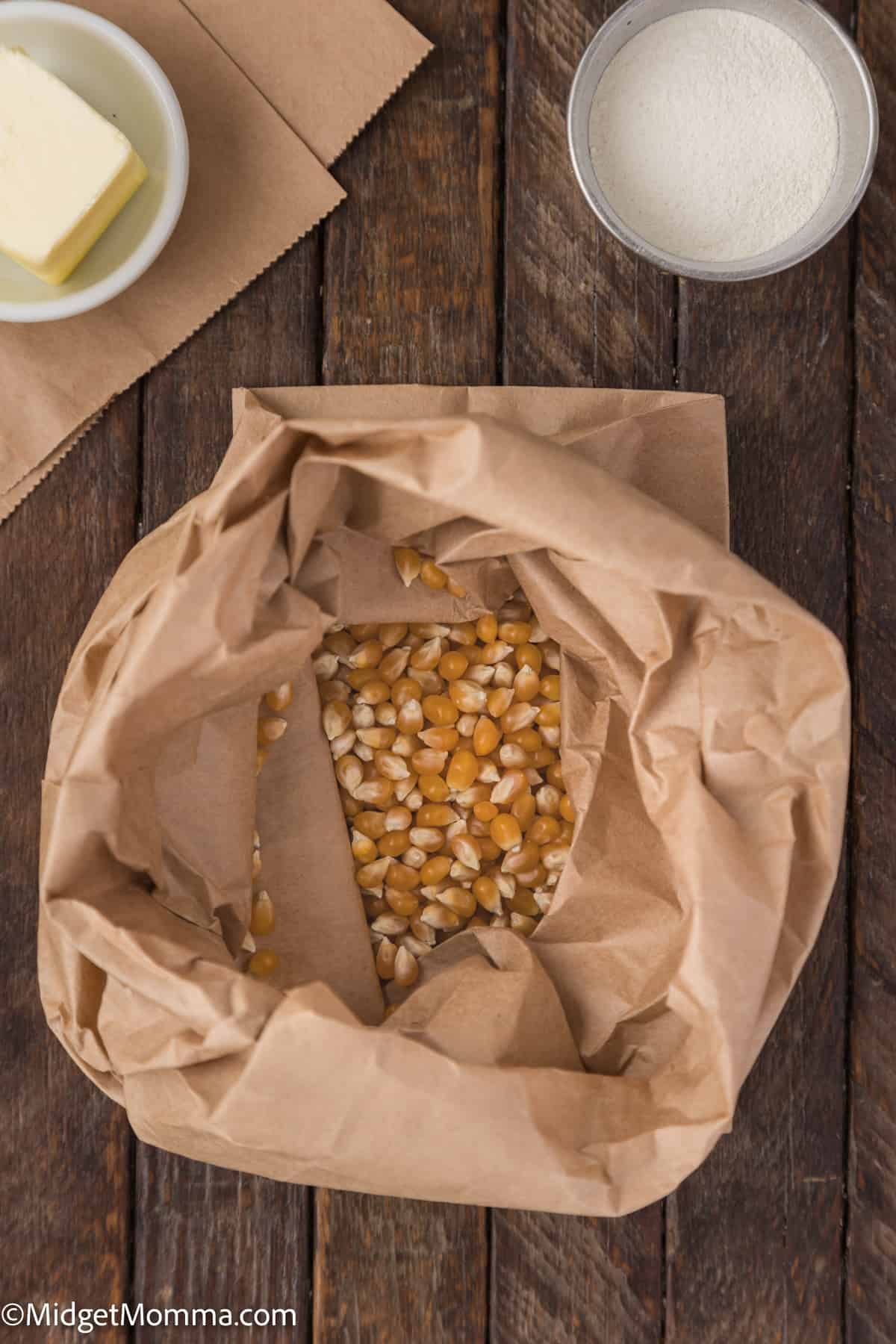 A brown paper bag of popcorn kernels on a wooden table.