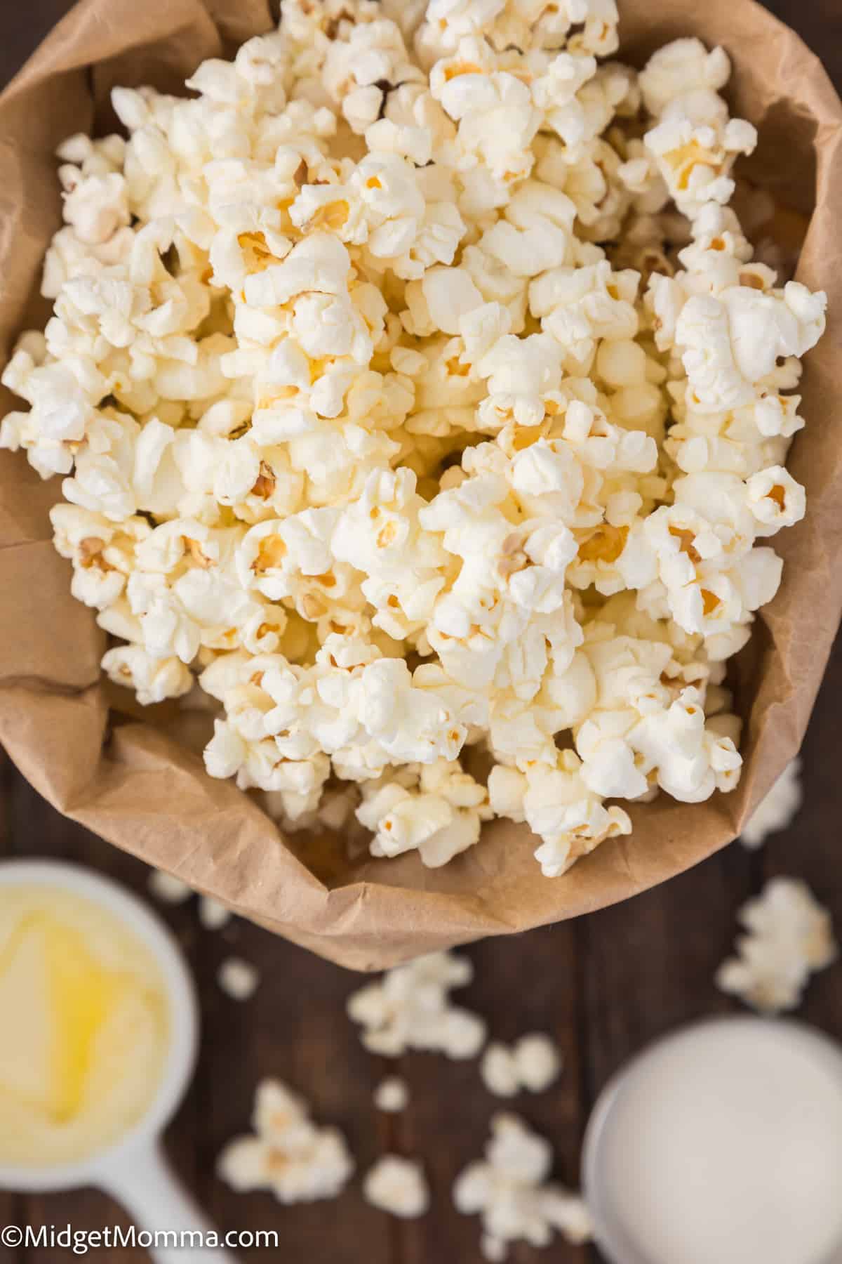 A bag of popcorn with some kernels spilled over, accompanied by a bowl of butter.