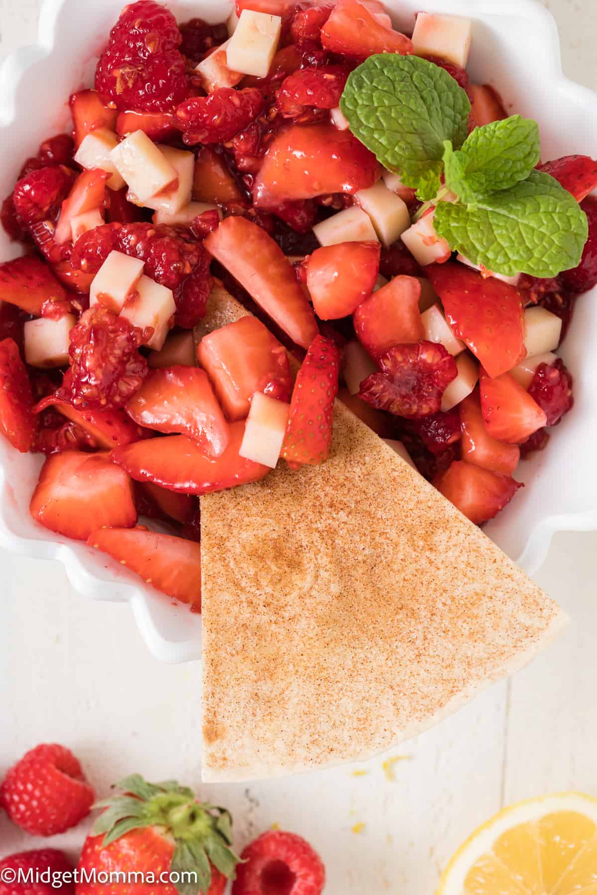 a bowl of fruit salsa with strawberries and raspberries with a cinnamon tortilla chip being dipped in