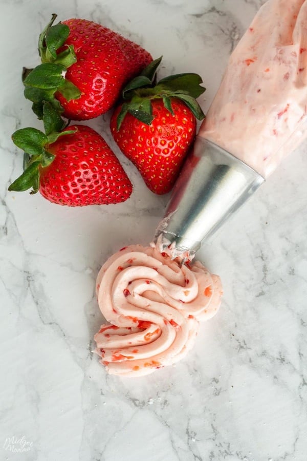 piping bag filled with low carb strawberry buttercream frosting next to strawberries on the counter.