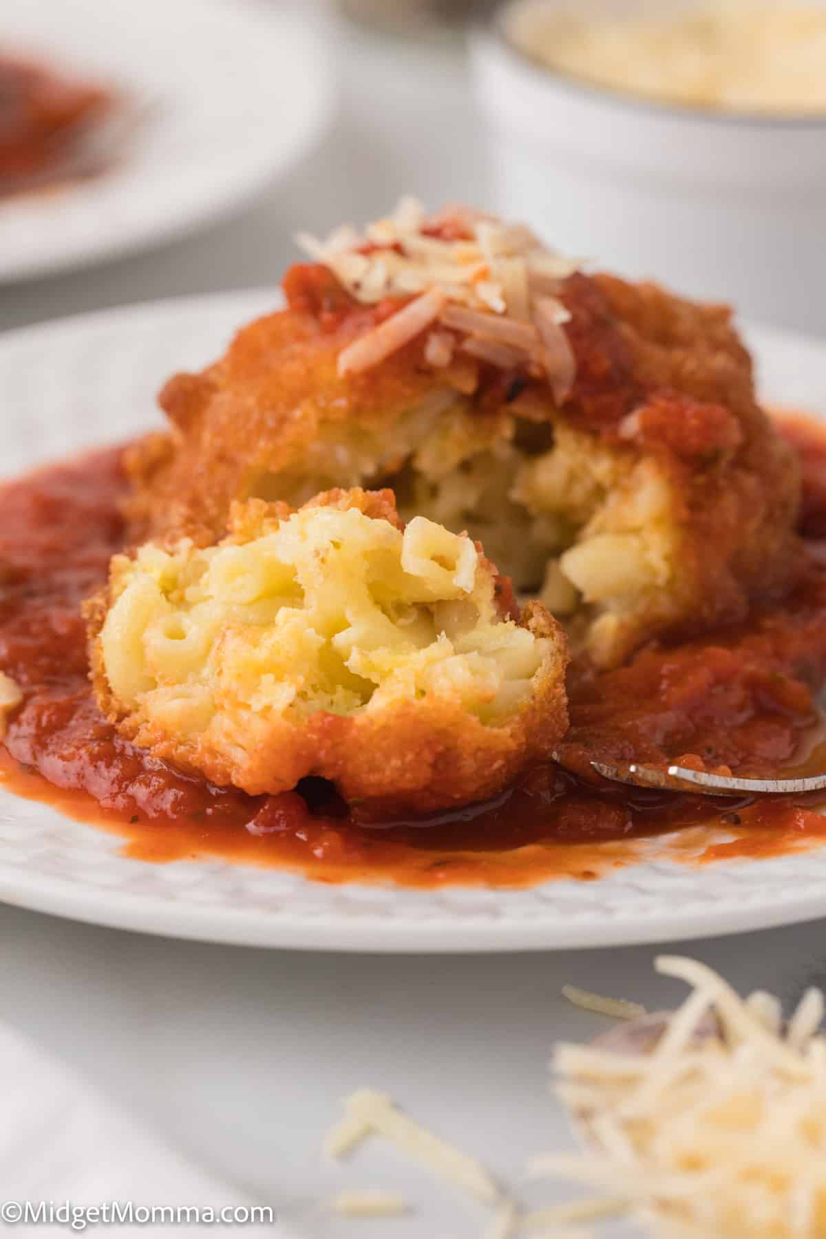 A white plate with a fried mac and cheese ball topped with sauce and shredded cheese close up photo.