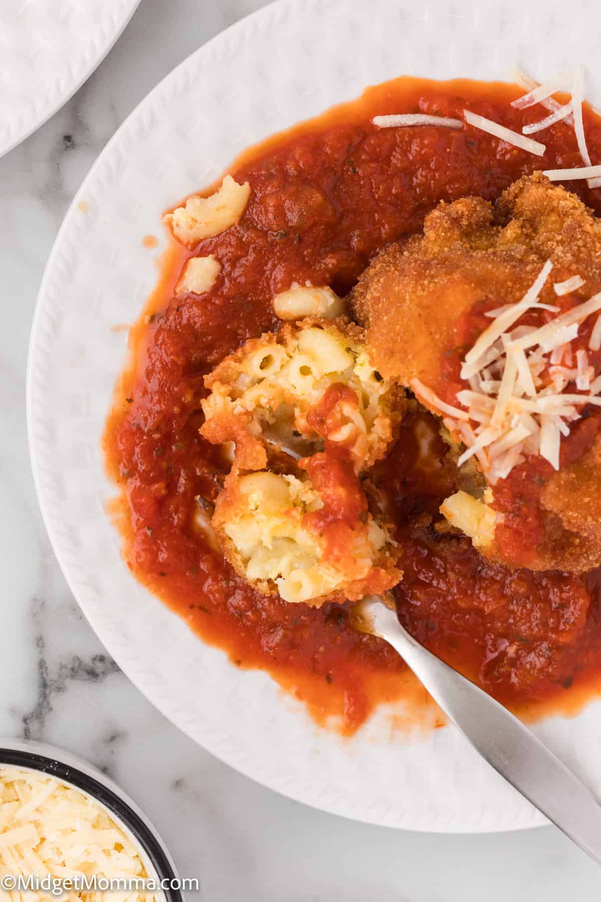 Over head photo of a white plate with a fried mac and cheese ball topped with sauce and shredded cheese.