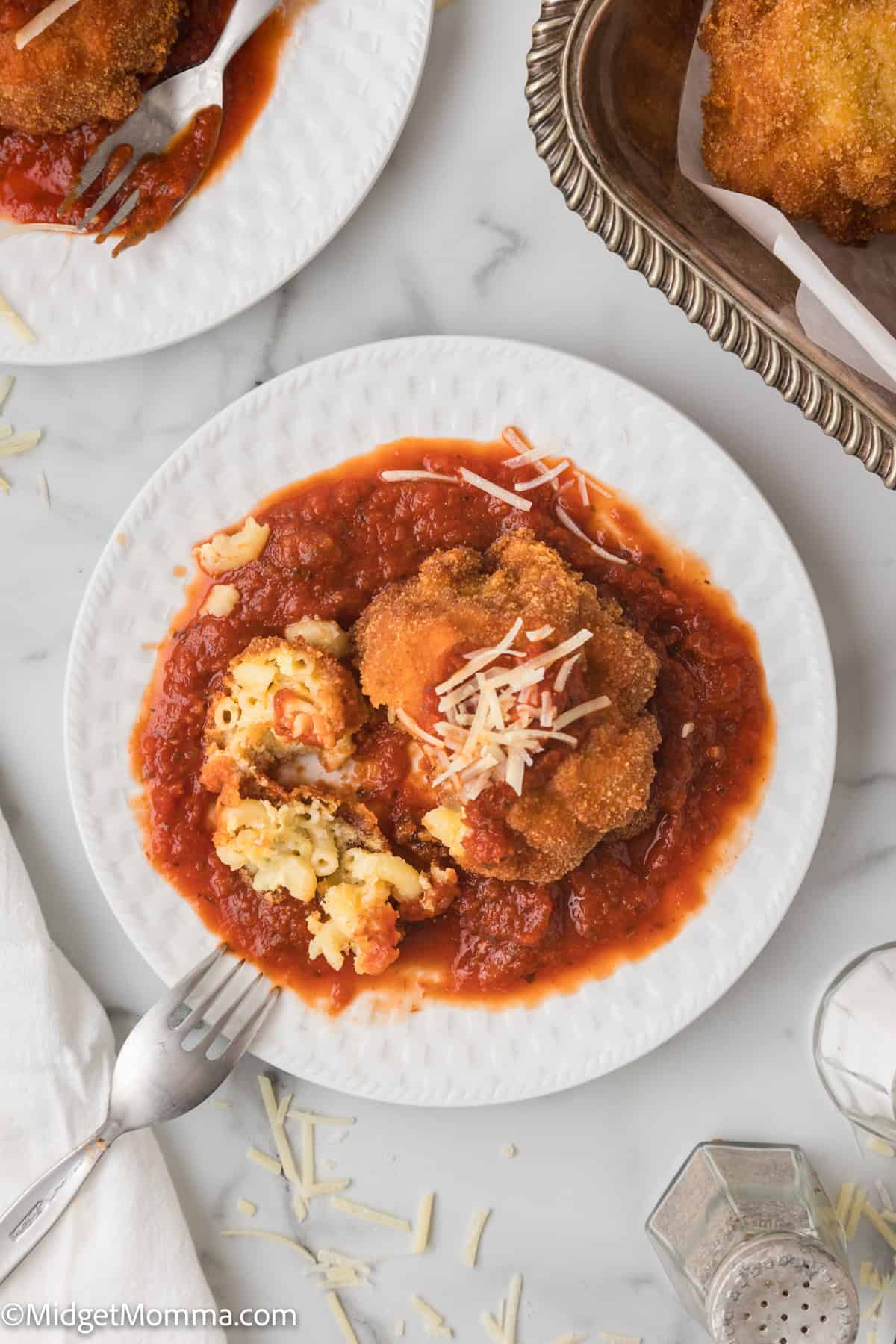 A white plate with a fried mac and cheese ball topped with sauce and shredded cheese.