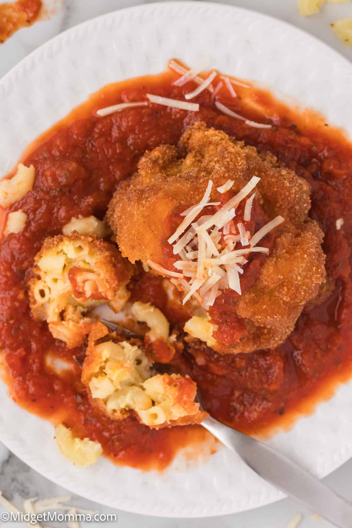 A plate of macaroni and cheese balls with marinara sauce, topped with shredded cheese, served on a white plate 