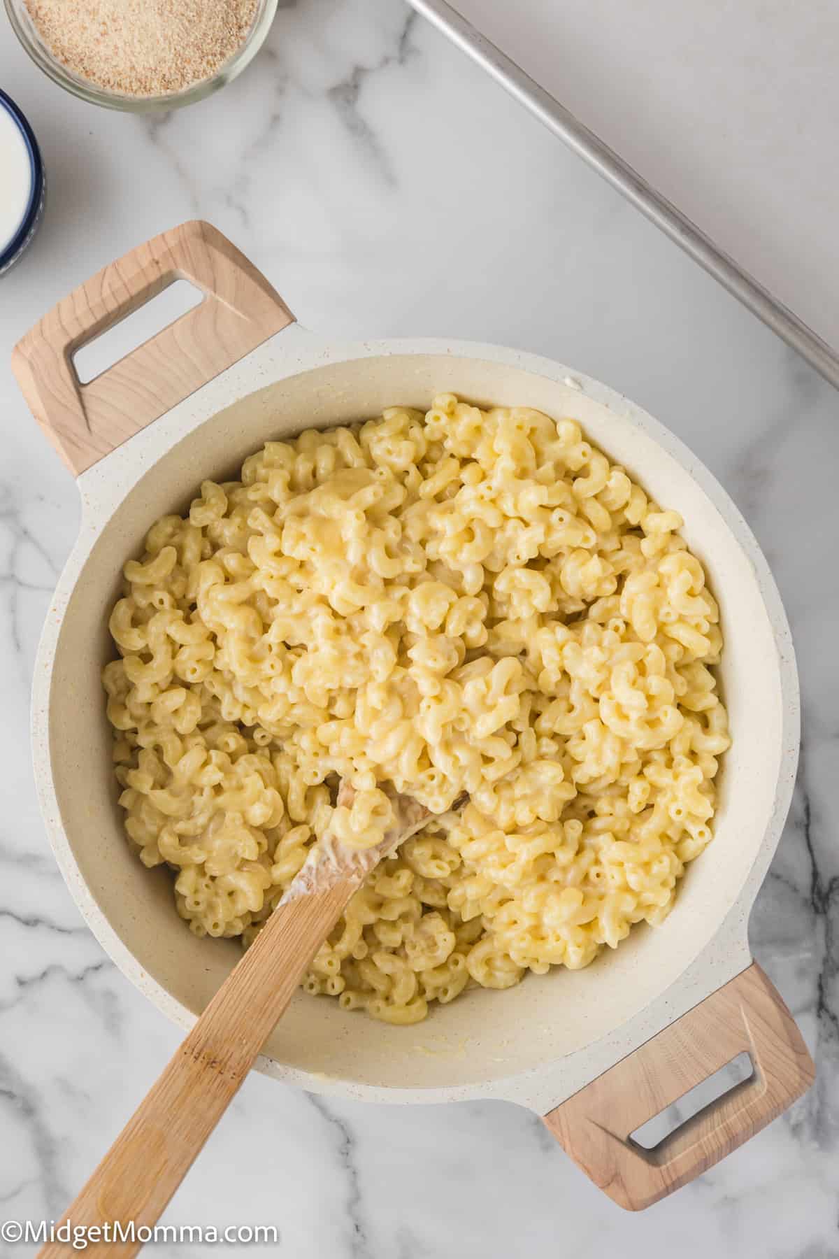 A pot of creamy macaroni and cheese on a kitchen counter, with a wooden spoon.