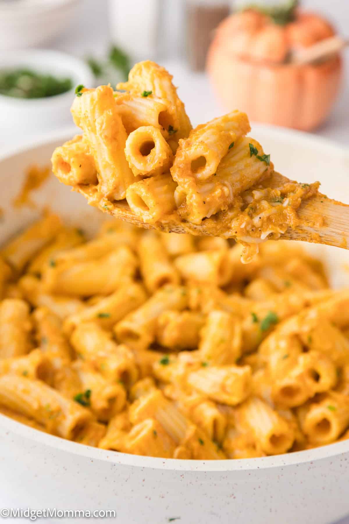 A close-up of a spoon lifting creamy pasta from a white bowl, garnished with parsley.