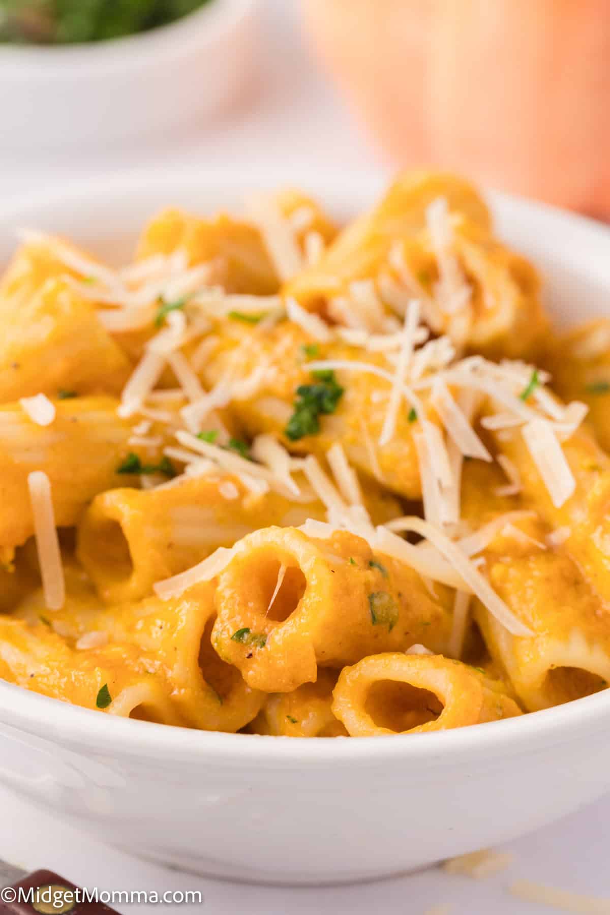 A bowl of creamy pumpkin pasta topped with grated parmesan cheese and parsley.