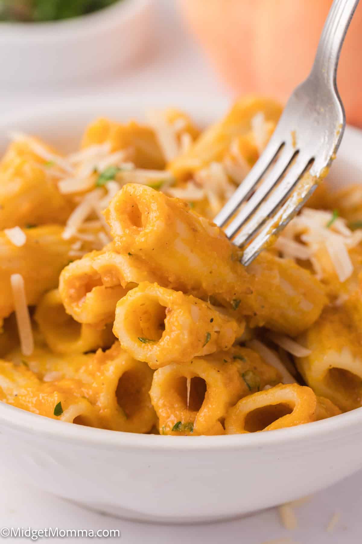 A fork lifts a serving of creamy pasta with pumpkin pasta sauce, garnished with parsley and grated cheese, with a blurred background.