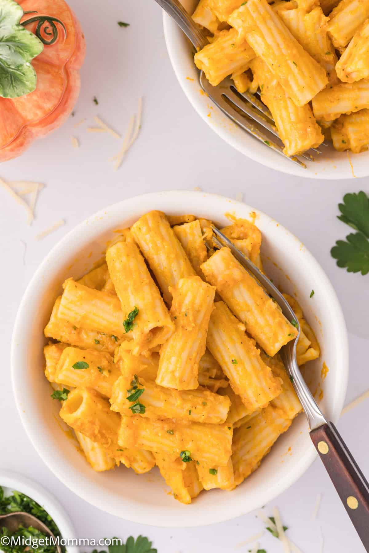 A bowl of creamy rigatoni pasta garnished with parsley, with a fork on the side.