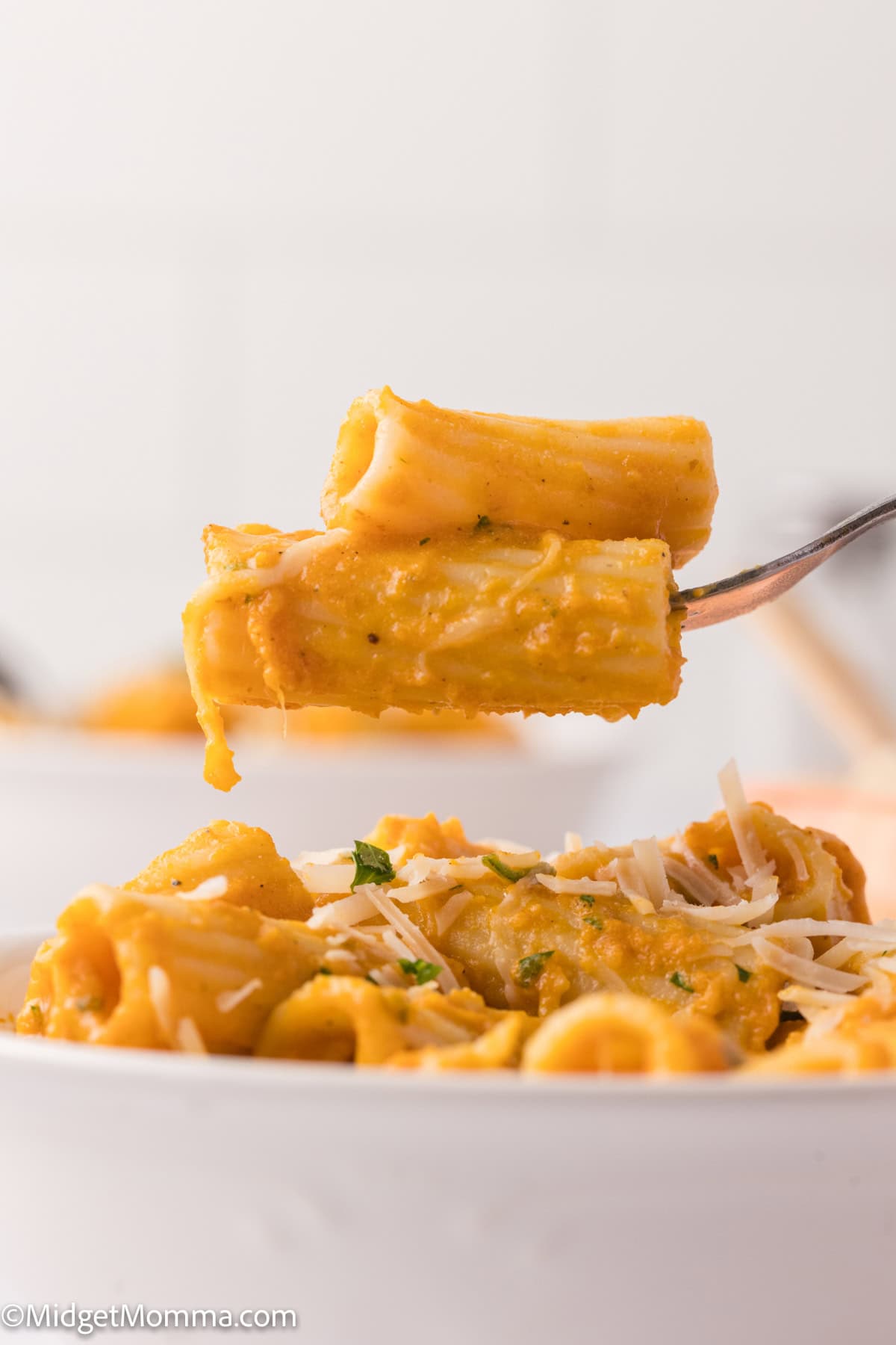 A fork lifting pasta covered with pumpkin pasta sauce, garnished with herbs.