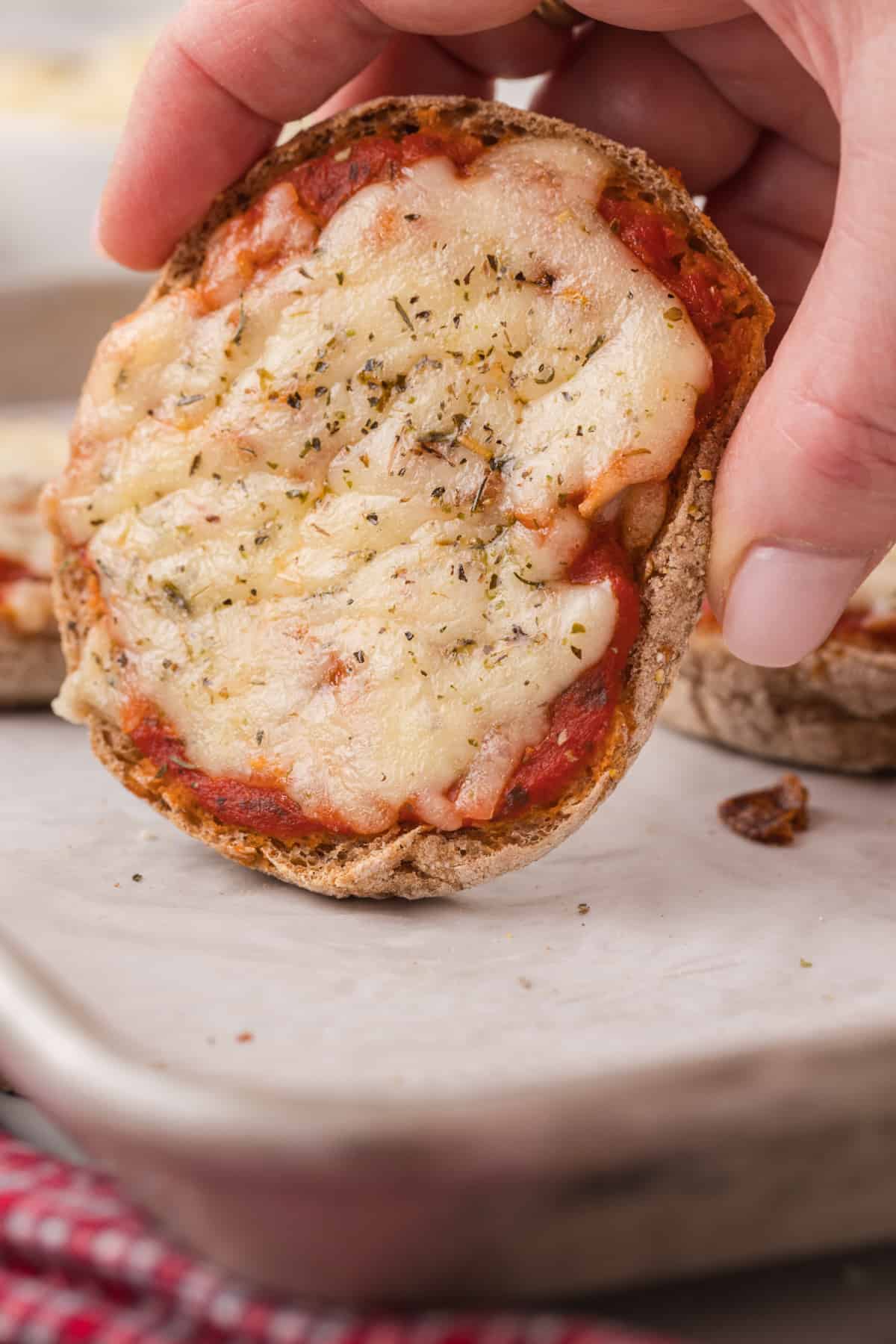 A person holding a english pizza on a baking sheet.