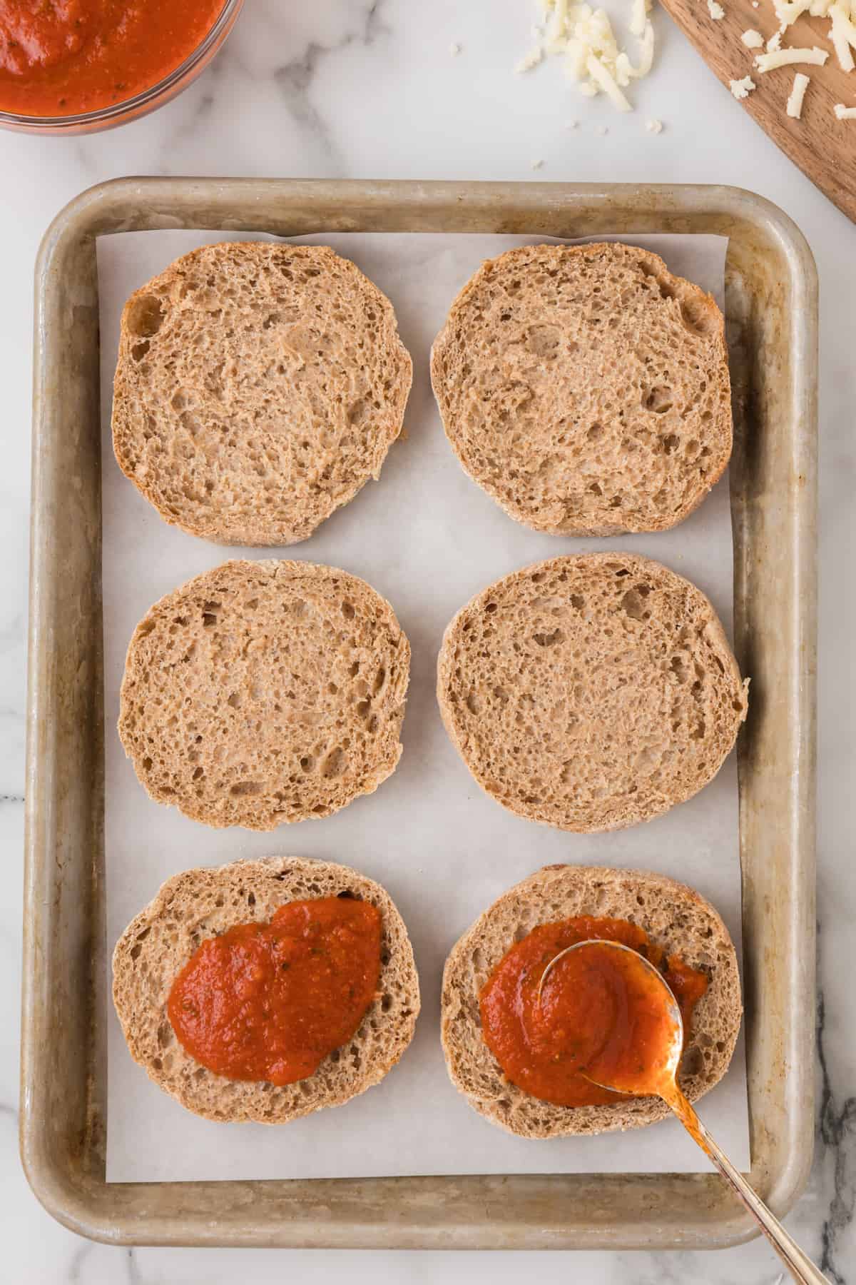 english muffin halves on a baking sheet topped with pizza sauce