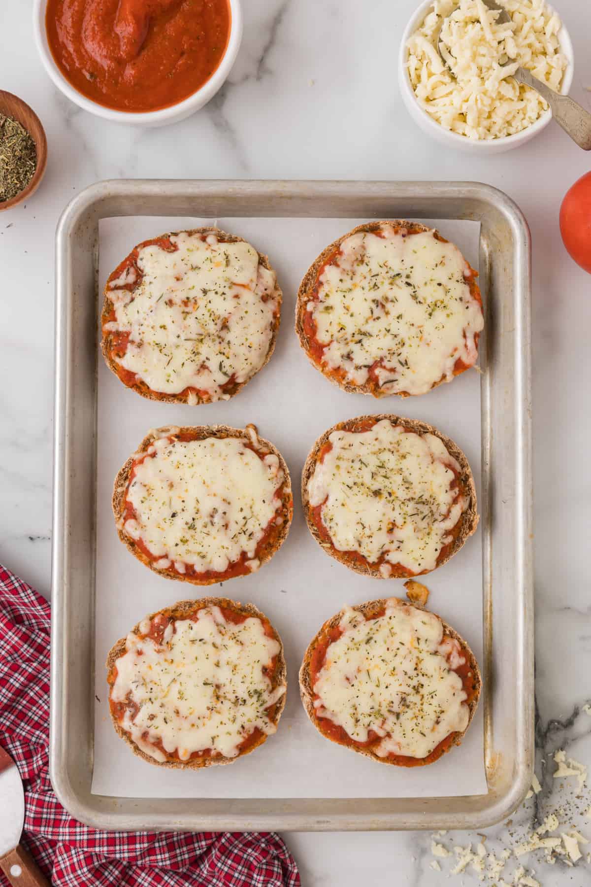 A baking sheet with mini pizzas made with english muffins on it.