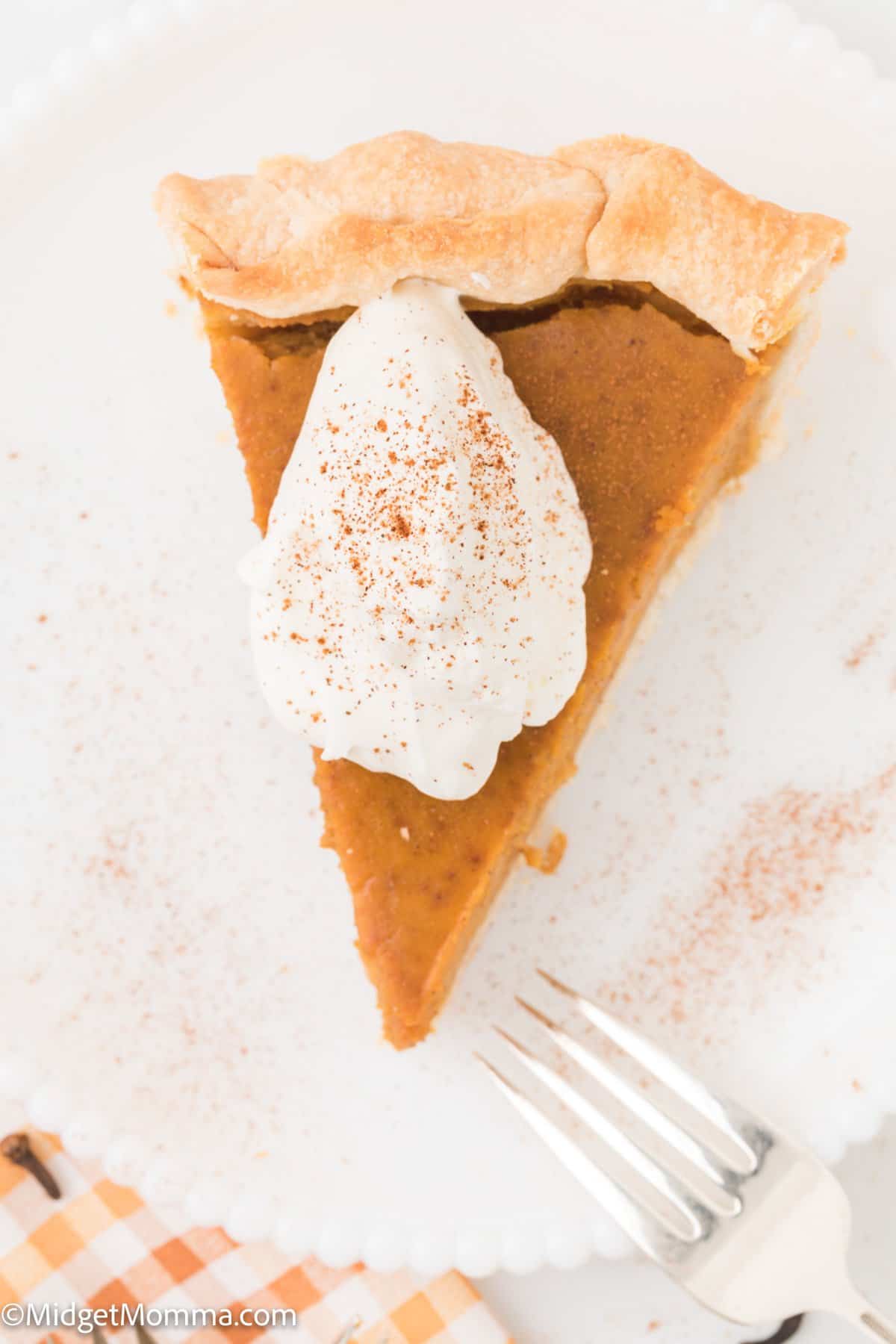 overhead photo of piece of pumpkin pie from scratch on a while plate topped with homemade whipped cream