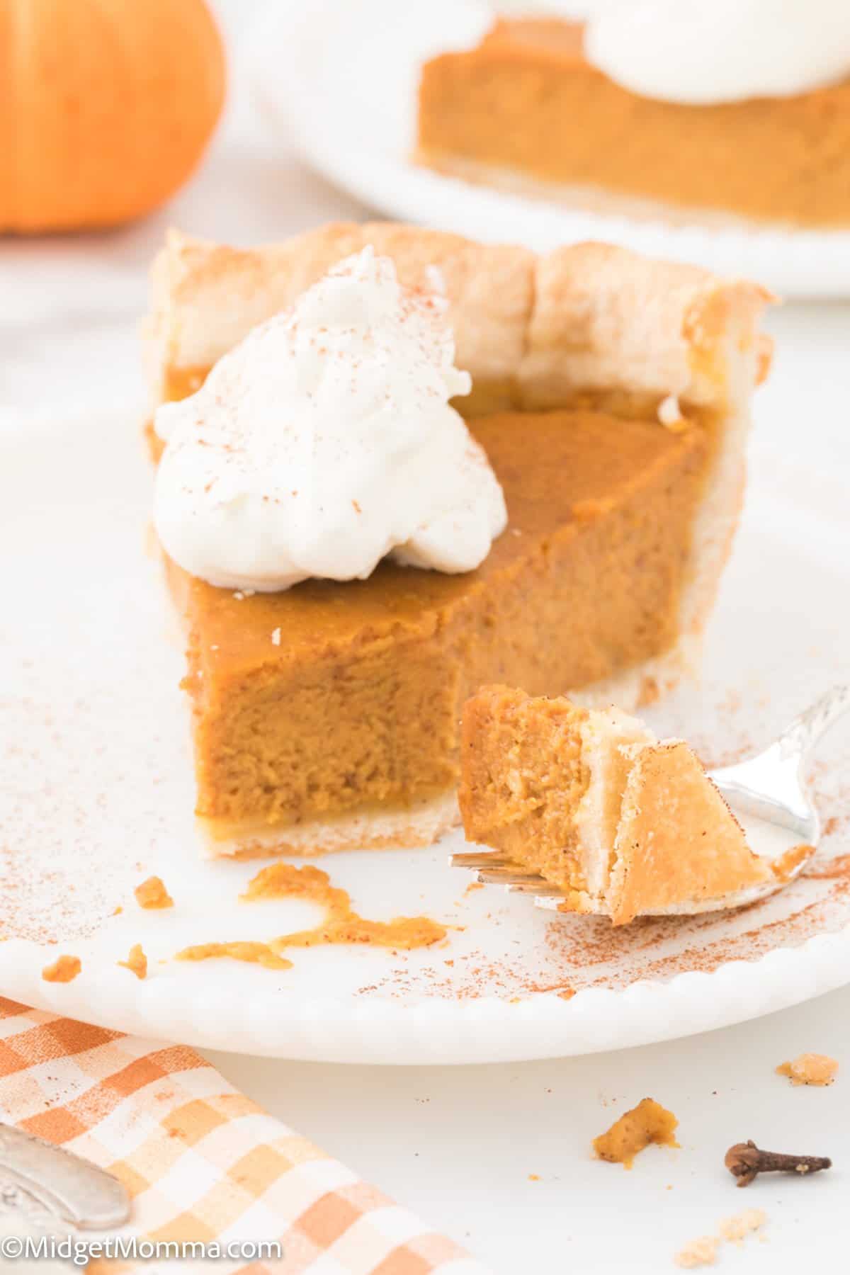 slice of homemade pumpkin pie topped with a dollop of whipped cream on a plate.