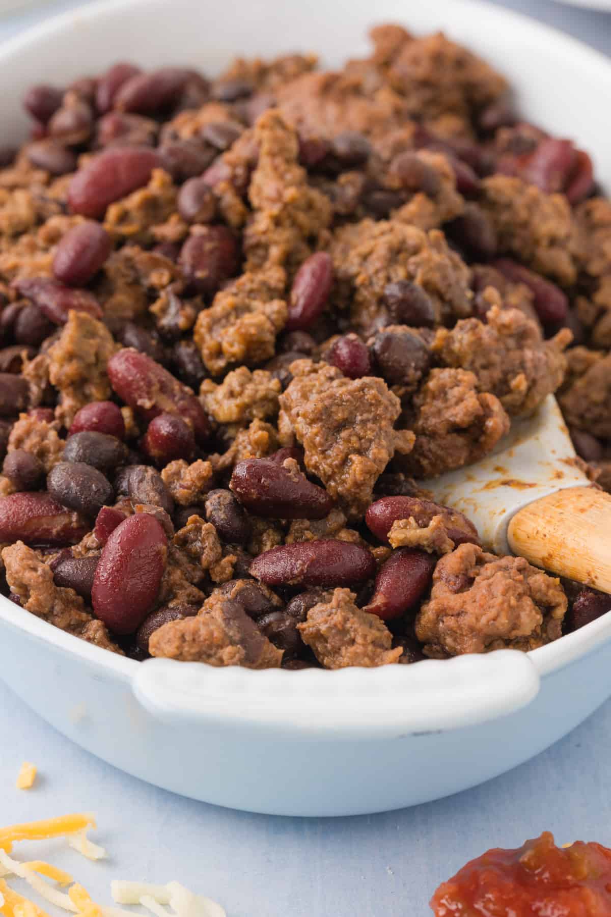 A bowl of slow cooker meat and beans with a wooden spoon.