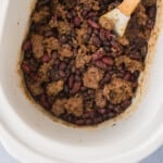 A crock pot full of meat and beans with a wooden spoon.