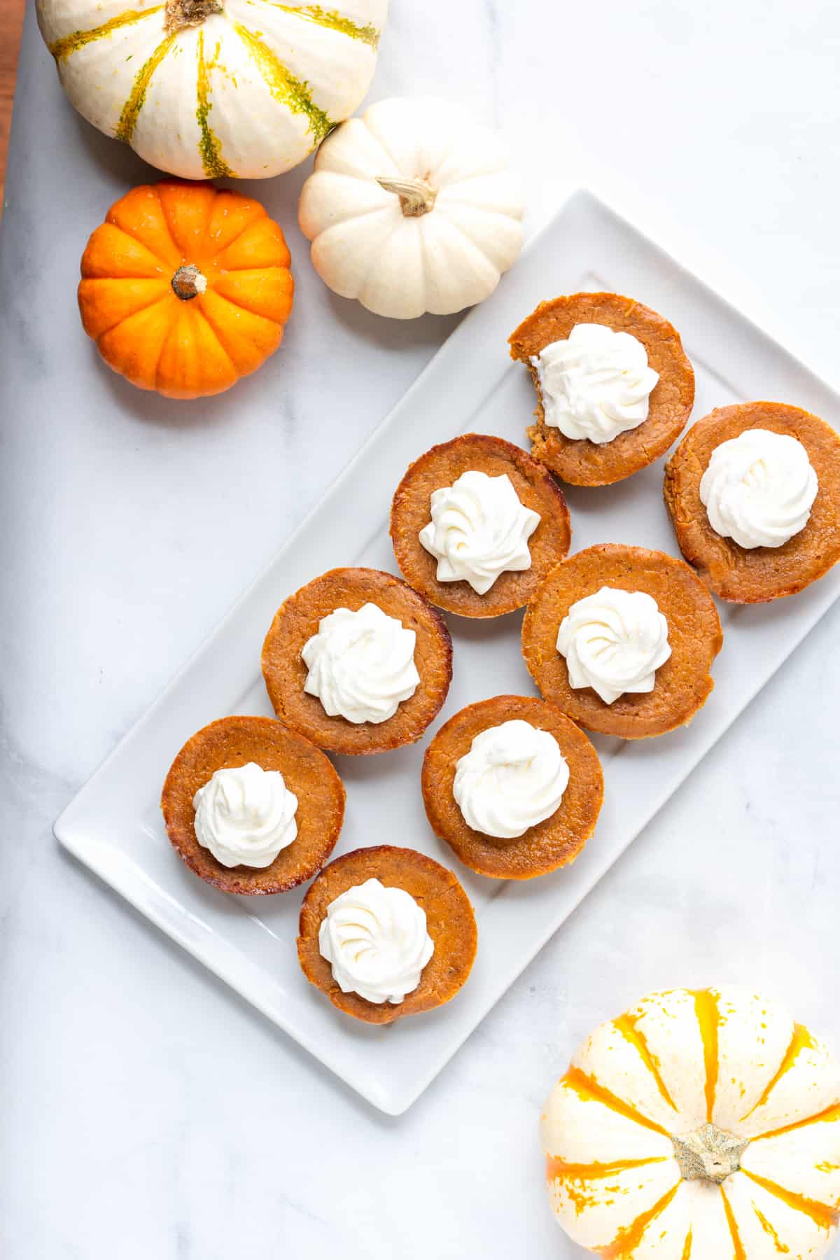 Pumpkin mini pies on a white plate surrounded by pumpkins.