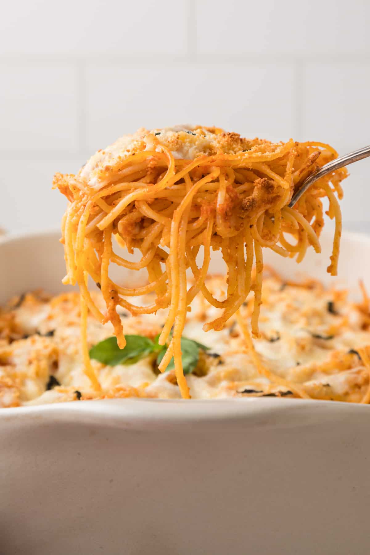 A spoonful of baked spaghetti pasta casserole  is being lifted out of a casserole dish.