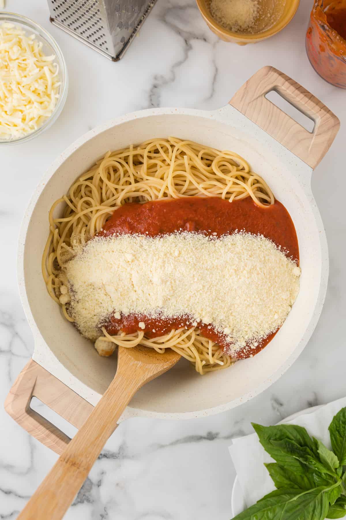 Spaghetti in a bowl with sauce and cheese and a wooden spoon mixing it.