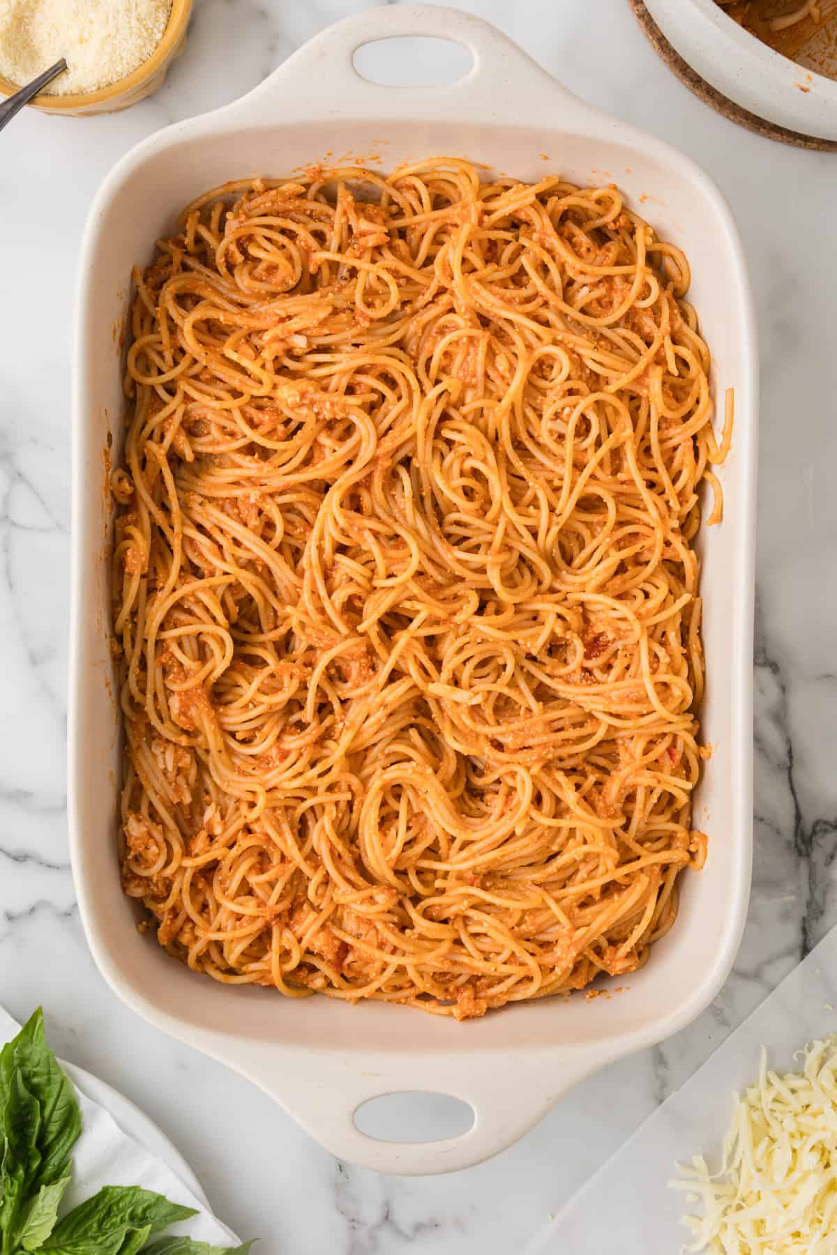 A dish of spaghetti with sauce and herbs on a marble countertop.