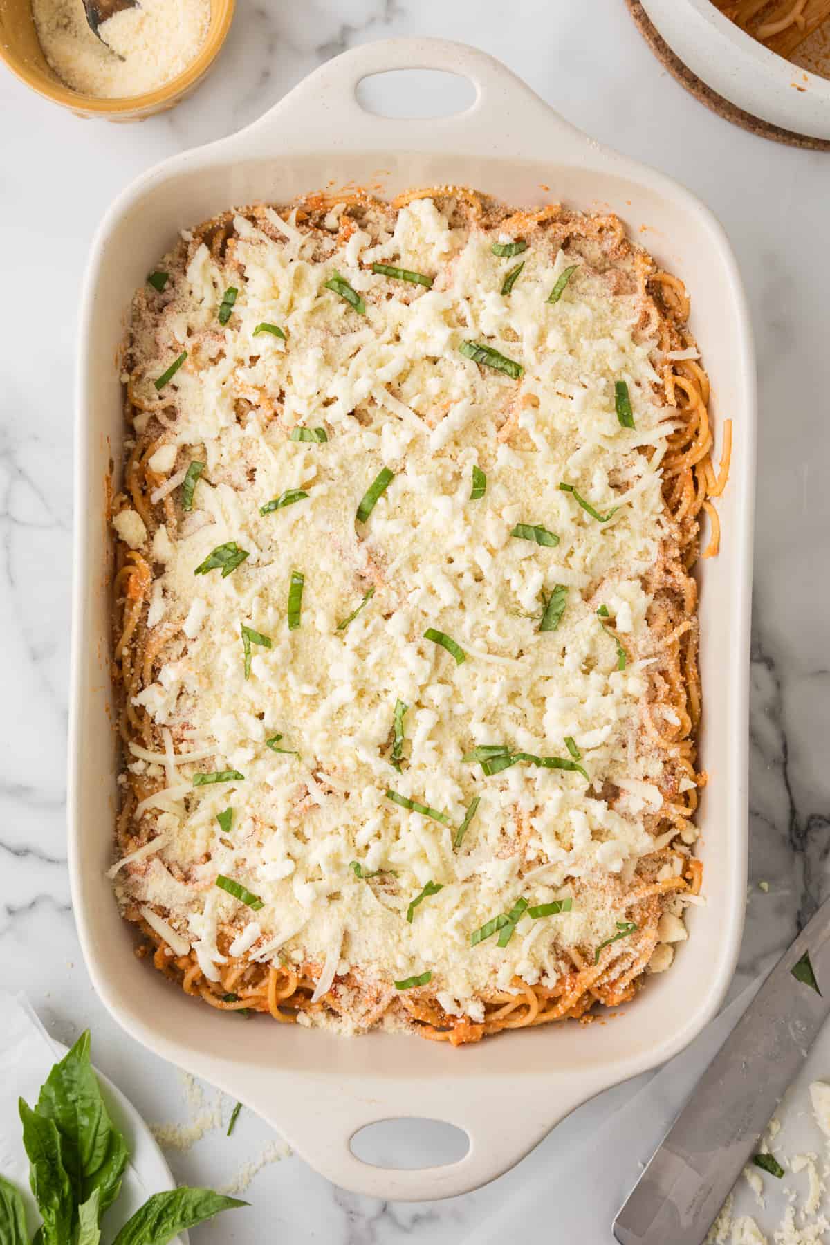 A casserole dish filled with spaghetti and parmesan ready to go in the oven.