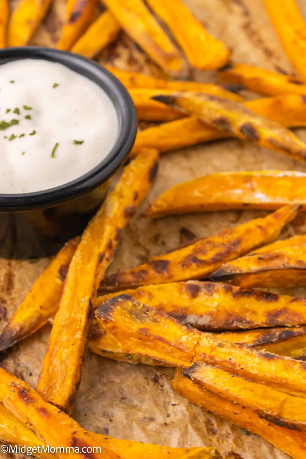 Sweet potato fries on parchment paper with a side of dipping sauce.