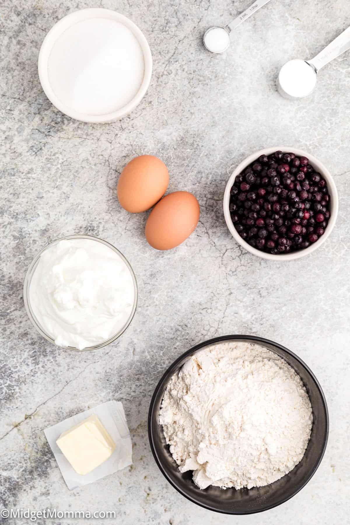 greek yogurt blueberry muffins recipe ingredients - eggs, bowls with flour, greek yogurt, butter, salt, baking powder, white sugar and blueberries