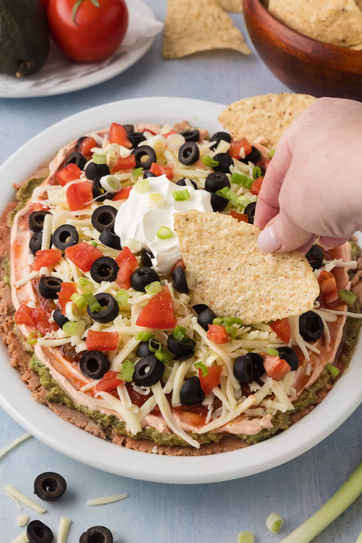 A person is dipping a tortilla into a 7 layer dip.