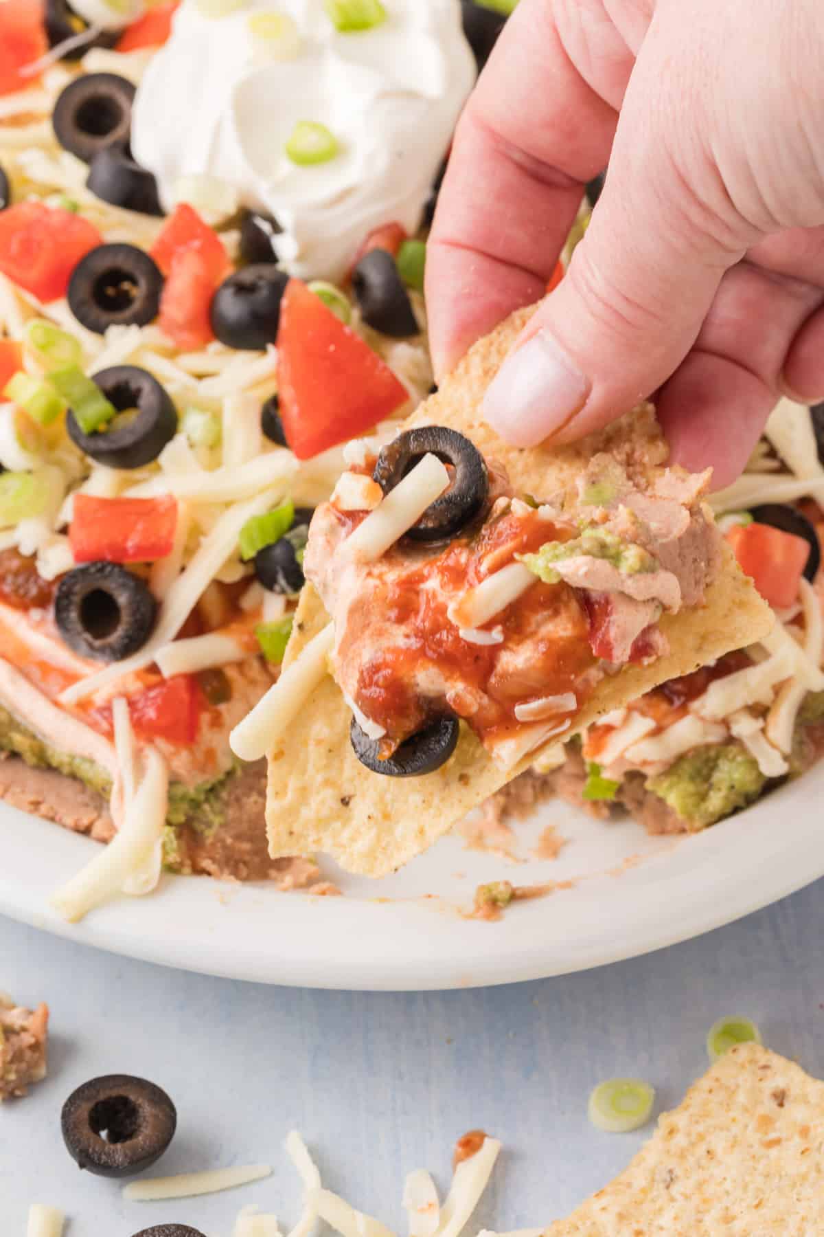 A person grabbing a bite of 7 layer dip with a tortilla chip.