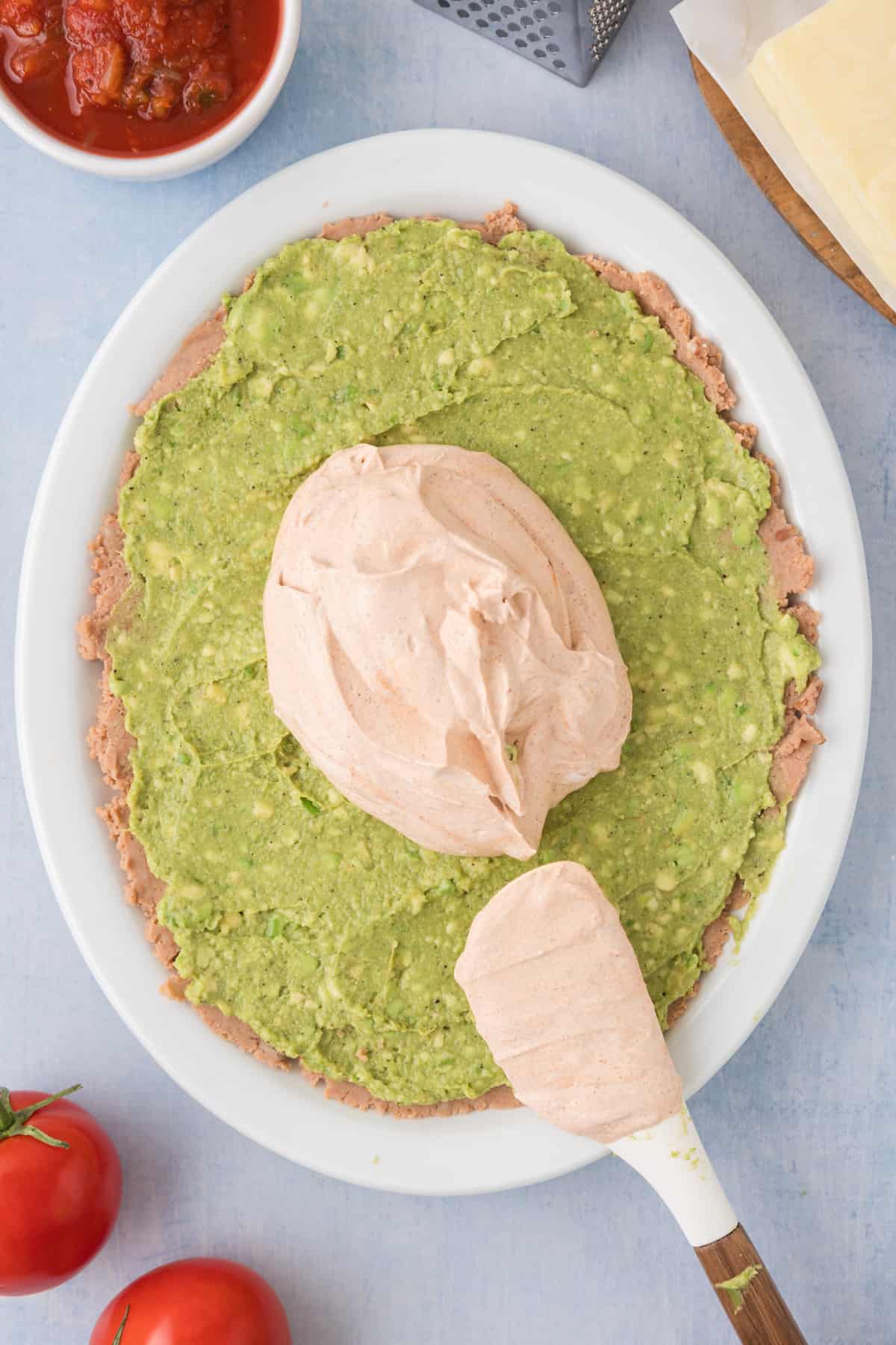 sour cream and taco seasoning mixture being spread on top of smashed avocados
