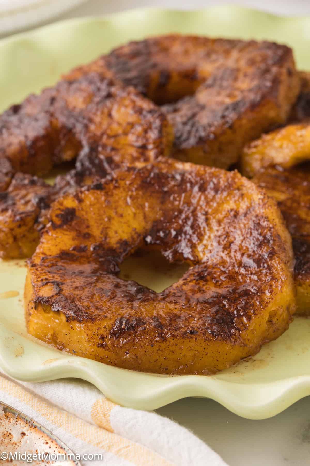 baked cinnamon sugar-coated pineapple rings served on a pale green plate.