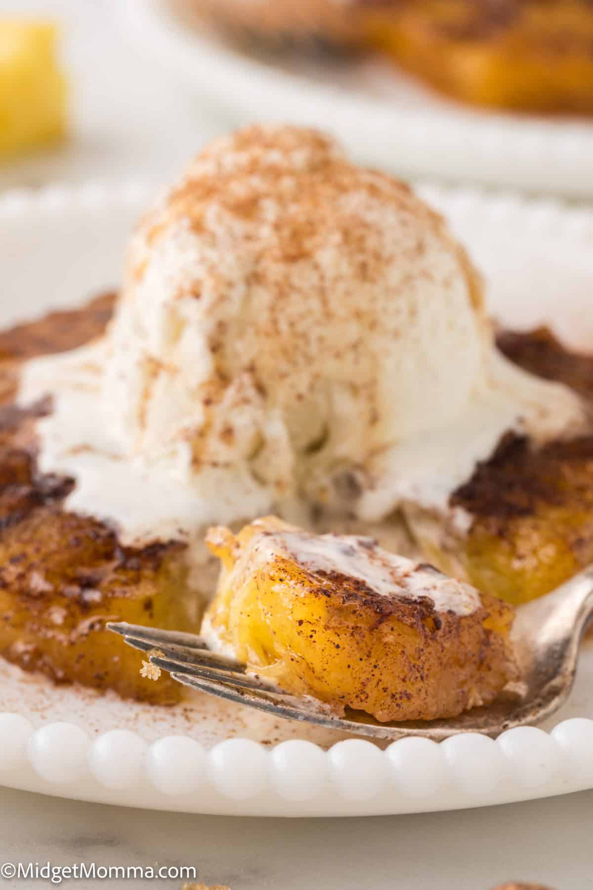 A serving of baked pineapple topped with a scoop of vanilla ice cream and sprinkled with cinnamon on a white plate.