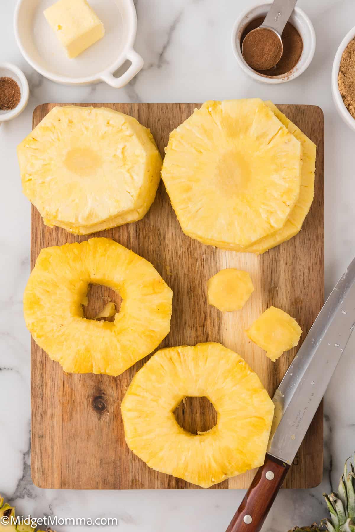 Sliced pineapple rings on a wooden cutting board next to a knife.