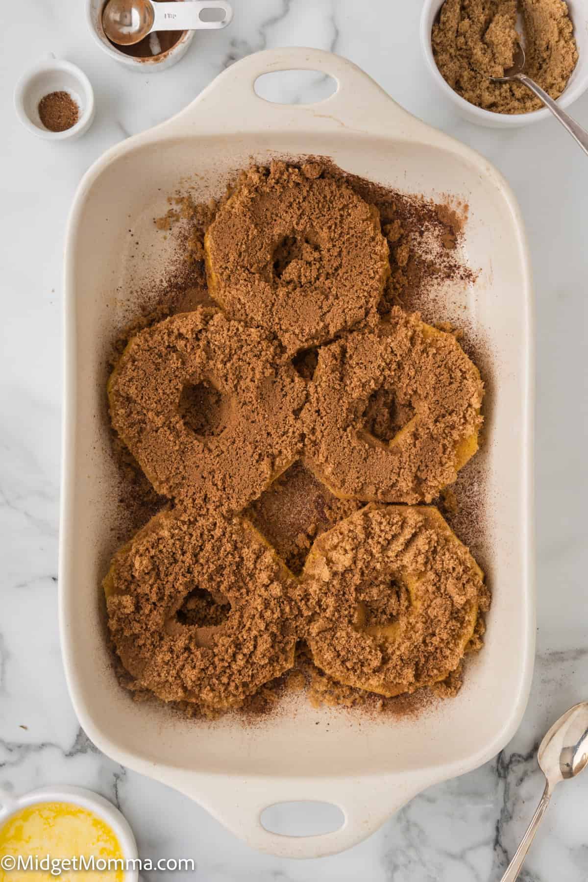 pineapple slices covered in cinnamon and brown sugar in a white ceramic dish on a marble countertop.