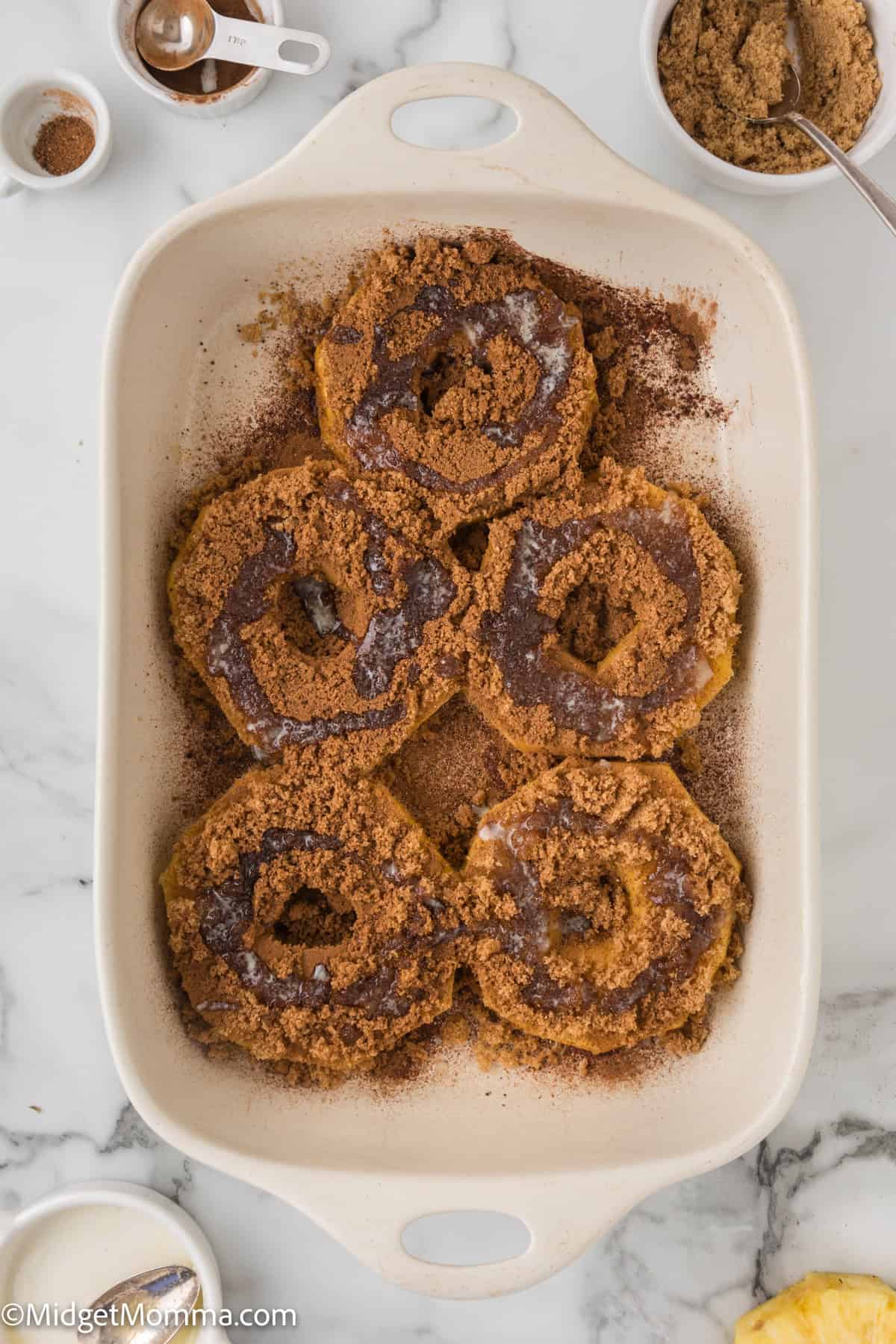 pineapple slices covered in cinnamon and brown sugar and butter poured on top in a white ceramic dish on a marble countertop.