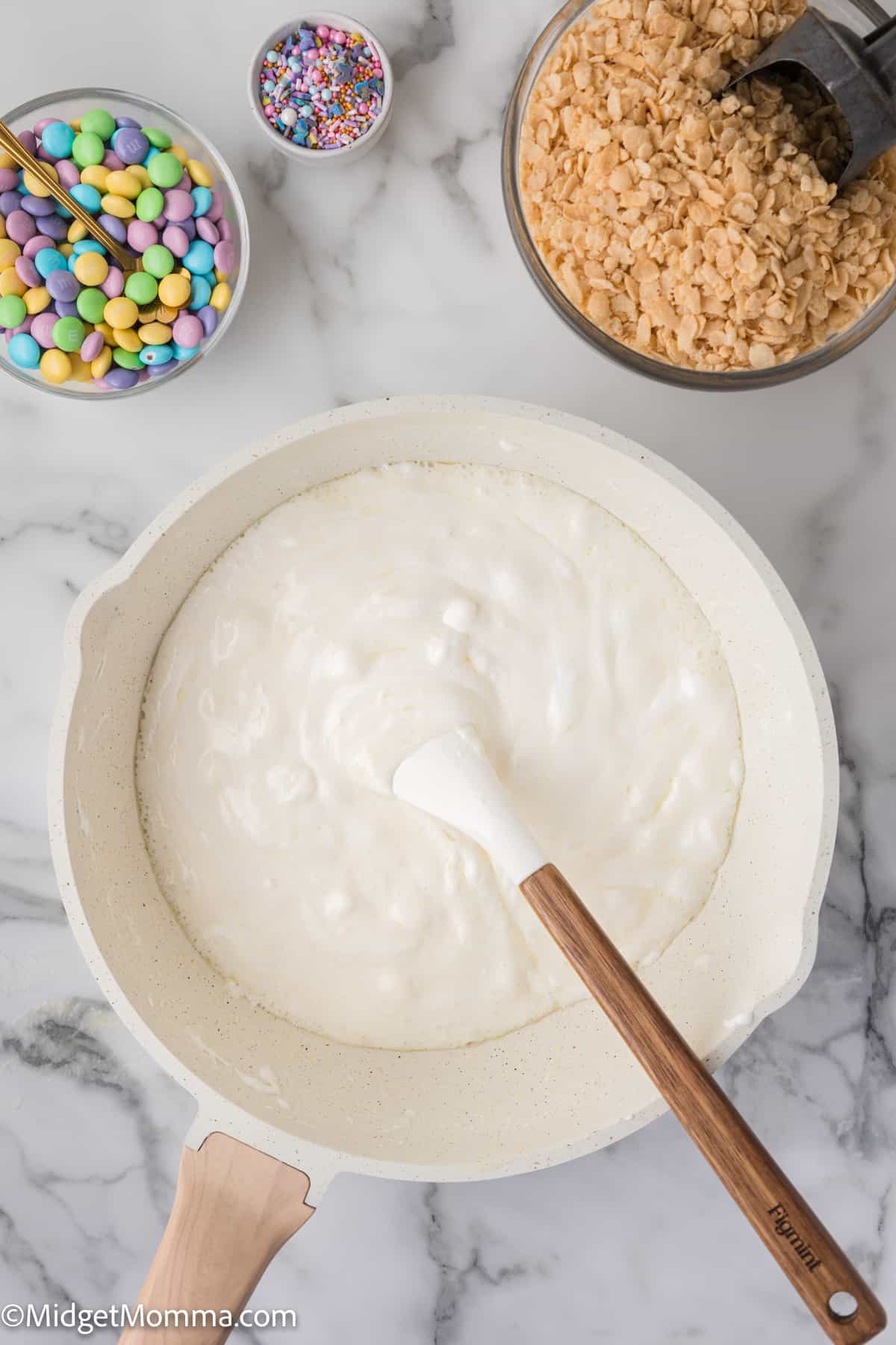 Mixing marshmallow and butter mixture in preparation for making rice krispie treats with ingredients on the side.