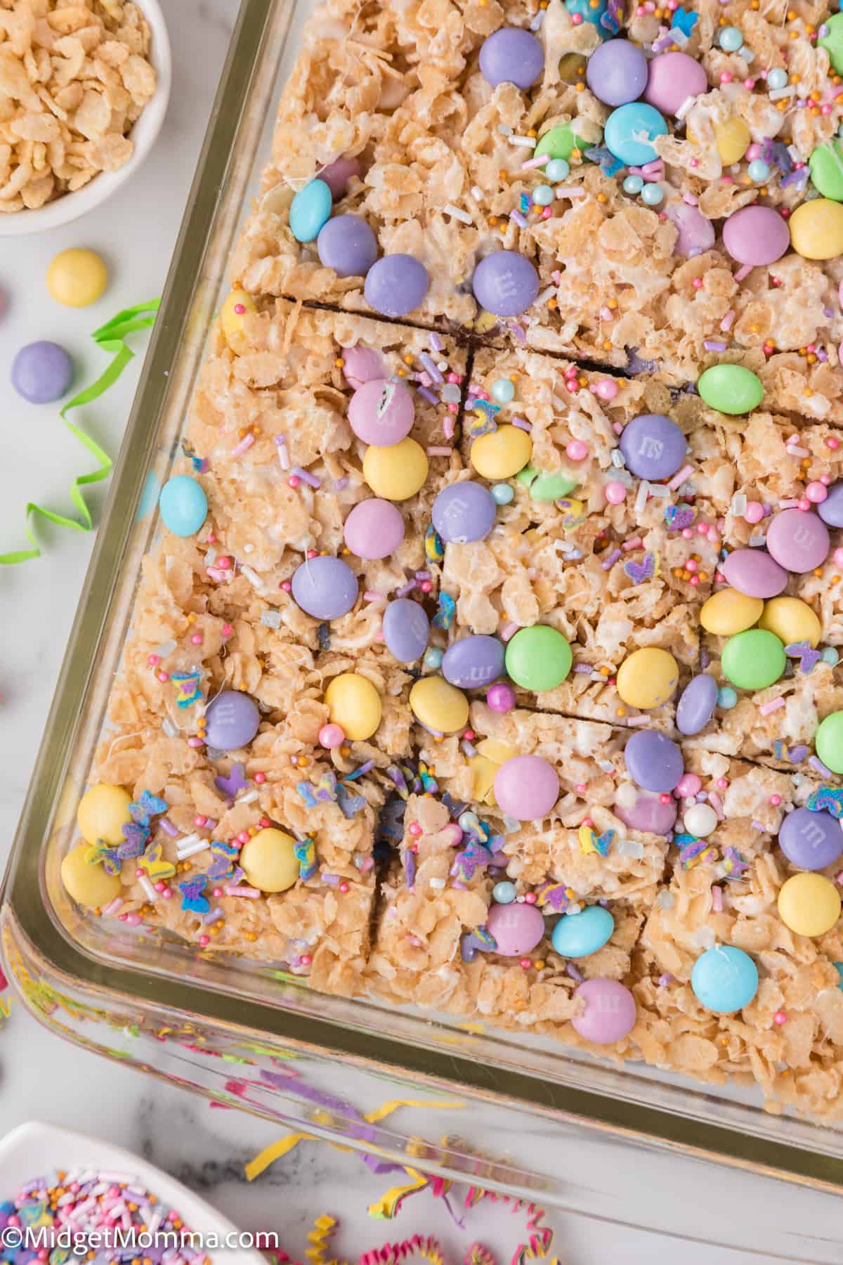 A festive tray of rice cereal treats sprinkled with colorful candy and edible glitter, ideal for a celebration.
