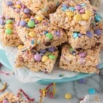 A stack of rice cereal treats decorated with colorful sprinkles and candy on a blue plate, suggesting a festive occasion.