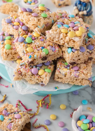 A stack of rice cereal treats decorated with colorful sprinkles and candy on a blue plate, suggesting a festive occasion.